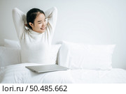 That woman sat on the bed, raised her hand, and put the laptop on the pillow. Стоковое фото, агентство Ingram Publishing / Фотобанк Лори