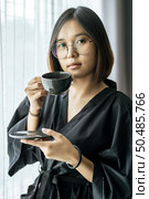 The woman wore a black robe near the window and drank coffee in the bedroom. Стоковое фото, агентство Ingram Publishing / Фотобанк Лори