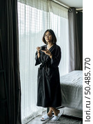 The woman wore a black robe near the window and drank coffee in the bedroom. Стоковое фото, агентство Ingram Publishing / Фотобанк Лори