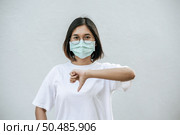The woman is wearing a mask and pointing her thumb down. Стоковое фото, агентство Ingram Publishing / Фотобанк Лори