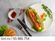 Top view hotdog placed in white dish beautifully with  carrot and lettuce, tomato sauce, fork and knife on floor, copy space. Стоковое фото, агентство Ingram Publishing / Фотобанк Лори