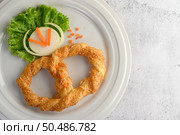 Top view Freshly baked soft pretzel with generous sprinkling of coarse salt and sesame on white dish, decorate with lettuce and carrot beautifully, copy space. Стоковое фото, агентство Ingram Publishing / Фотобанк Лори