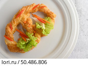 Top view Freshly baked soft pretzel with generous sprinkling of coarse salt and sesame on white dish, decorate with lettuce and carrot beautifully, copy space. Стоковое фото, агентство Ingram Publishing / Фотобанк Лори