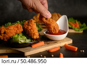 Hand holding crispy fried chicken dipped in tomato sauce. Selective focus. Стоковое фото, агентство Ingram Publishing / Фотобанк Лори