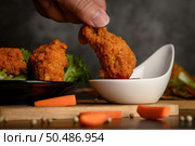Hand holding crispy fried chicken dipped in tomato sauce. Selective focus. Стоковое фото, агентство Ingram Publishing / Фотобанк Лори