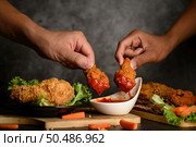 Two hand holding crispy fried chicken dipped in tomato sauce.Selective focus. Стоковое фото, агентство Ingram Publishing / Фотобанк Лори