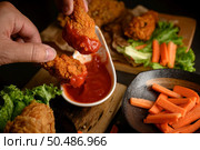 Hand holding crispy fried chicken dipped in tomato sauce. Selective focus. Стоковое фото, агентство Ingram Publishing / Фотобанк Лори