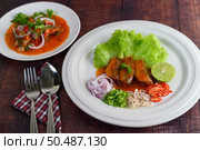 Selective focus Spicy salad of sardine with tomato sauce arranged nicely in white dish and mixed with herb blurred nearly, the sparken stainless spoon and fork over napkin on wooden table, copy space. Стоковое фото, агентство Ingram Publishing / Фотобанк Лори