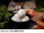 Boiled eggs in a black bowl, garlic, sausage, tomatoes placed on a wooden cutting board. Стоковое фото, агентство Ingram Publishing / Фотобанк Лори