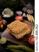 Noodles on a wooden cutting board with tomato, lime, spring onion, chili and baby corn. Стоковое фото, агентство Ingram Publishing / Фотобанк Лори