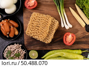 Noodles on a wooden cutting board with tomato, lime, spring onion, chili and baby corn. Стоковое фото, агентство Ingram Publishing / Фотобанк Лори