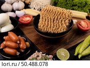 Noodles on a wooden cutting board with tomato, lime, spring onion, chili and baby corn. Стоковое фото, агентство Ingram Publishing / Фотобанк Лори