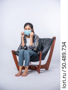 An uncomfortable woman sitting on a chair and wearing a mask. Стоковое фото, агентство Ingram Publishing / Фотобанк Лори