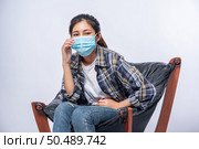 An uncomfortable woman sitting on a chair and wearing a mask. Стоковое фото, агентство Ingram Publishing / Фотобанк Лори