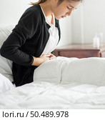 A woman sitting in bed with abdominal pain and pressing her hand on her stomach. Стоковое фото, агентство Ingram Publishing / Фотобанк Лори