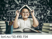 A boy with glasses studied and put a book on his head in the classroom. Стоковое фото, агентство Ingram Publishing / Фотобанк Лори