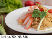 Stir-fried instant noodle with prawn and crab stick along with tomatoes and peppers in a white plate on a wooden floor. Стоковое фото, агентство Ingram Publishing / Фотобанк Лори