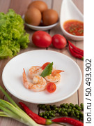 Three fresh shrimp and half tomatoes in a white plate on a wooden. Стоковое фото, агентство Ingram Publishing / Фотобанк Лори