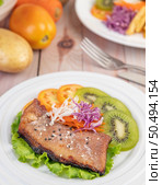 Fish steak with french fries, kiwi, lettuce, carrots, tomatoes, and cabbage in a white dish. Стоковое фото, агентство Ingram Publishing / Фотобанк Лори