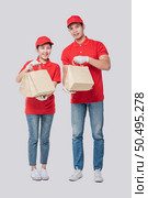 Image of a happy young delivery man in red cap blank t-shirt uniform standing with empty brown craft paper packet isolated on light gray background studio. Стоковое фото, агентство Ingram Publishing / Фотобанк Лори
