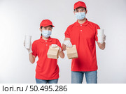 Image of a happy young delivery man in red cap blank t-shirt uniform face mask gloves standing with empty brown craft paper packet isolated on light gray background studio, Service during pandemic coronavirus virus covid-19 concept. Стоковое фото, агентство Ingram Publishing / Фотобанк Лори