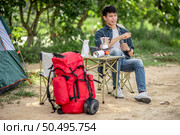 Young traveler man sitting at front of the tent in forest while camping trip on summer vacation with coffee set . Стоковое фото, агентство Ingram Publishing / Фотобанк Лори