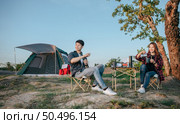 Cheerful Young backpacker couple sitting at front of the tent in forest with coffee set and making fresh coffee grinder while camping trip on summer vacation. Стоковое фото, агентство Ingram Publishing / Фотобанк Лори