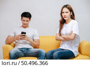 young couple arguing while handsome man using mobile phone on sofa in living room at home. husband addict On Mobile Phone Ignoring her, upset couple, family issues and relationship concept. Стоковое фото, агентство Ingram Publishing / Фотобанк Лори