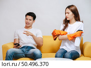 Asian young couple quarrels while cleaning in the living room, Young woman wearing gloves and holding spray bottle in hand with feel dissatisfied her husband, family issues and relationship concept. Стоковое фото, агентство Ingram Publishing / Фотобанк Лори