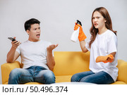 Asian young couple quarrels while cleaning in the living room, Young woman wearing gloves and holding spray bottle in hand with feel dissatisfied her husband, family issues and relationship concept. Стоковое фото, агентство Ingram Publishing / Фотобанк Лори