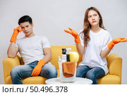 Asian young couple quarrels while cleaning in the living room, They are sitting on sofa and wearing gloves with feel dissatisfied together, family issues and relationship concept. Стоковое фото, агентство Ingram Publishing / Фотобанк Лори