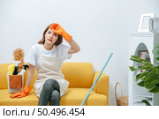 Young housekeeper woman sitting on sofa in living room with feel tired, She wipe sweat and take a break after finishing cleaning the house, copy space. Стоковое фото, агентство Ingram Publishing / Фотобанк Лори