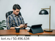 Happily Young handsome man with new normal, Stay at home and works from home on digital tablet and use smartphone during self-isolation and quarantine covid-19 coronavirus outbreak. Стоковое фото, агентство Ingram Publishing / Фотобанк Лори
