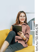 Young woman wearing glasses sitting on sofa and using technology of digital pen on tablet to working from home during self-isolation and quarantine covid-19 coronavirus outbreak. Стоковое фото, агентство Ingram Publishing / Фотобанк Лори