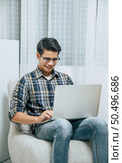 Young handsome man wearing eyeglasses with new normal, Stay at home and works from home on laptop computer while self-isolation and quarantine covid-19 coronavirus outbreak. Стоковое фото, агентство Ingram Publishing / Фотобанк Лори