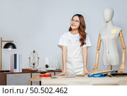 Portrait of young pretty female fashion designer stylish wearing eyeglasses standing and smile with proud during working at fashion studio, full of tailoring tools and equipment. Стоковое фото, агентство Ingram Publishing / Фотобанк Лори