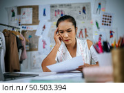 Portrait Young fashion designer female disappointed lost bored and seamstress at workshop, blured colors pencils, beautiful sketch on board in background. Стоковое фото, агентство Ingram Publishing / Фотобанк Лори