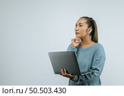 Portrait of Asian woman holding  laptop in hand and looking aside serious thinking, standing over background in studio with copy space. Advertising concept. Стоковое фото, агентство Ingram Publishing / Фотобанк Лори