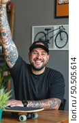 Tattooed lucky freelancer in front of his working space, surrounded with his hobby toys longboard, vintage bicycle and green plant, stretching his hand in air. Стоковое AI-видео, аниматор Sergey Grishin / Фотобанк Лори