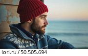 Young handsome man with beard wears traditional authentic blue wool knitted sweater with ornaments and red fisherman or sailor beanie hat, looks to horizon on fish boat. Стоковое AI-видео, аниматор Sergey Grishin / Фотобанк Лори