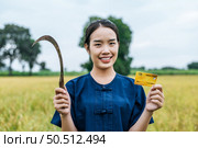 Portrait of asian young farmer woman showing credit card on rice field background, she hold sickle smile with happy in successful and rich. Стоковое фото, агентство Ingram Publishing / Фотобанк Лори