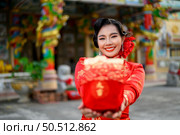 Portrait Asian beautiful woman wearing a cheongsam smiling and poses show Red amulet bag at shrine on Chinese New Year, copy space. Стоковое фото, агентство Ingram Publishing / Фотобанк Лори