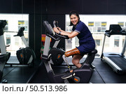 Young female with one prosthetic leg with exercising with a spinning bike in the gym to practice joint use with the other normal leg to be flexible, Concept of living a woman’s life with a prosthetic. Стоковое фото, агентство Ingram Publishing / Фотобанк Лори