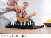 In the living room of the house, an elderly couple sits and relaxes. to begin playing chess together with a chess board with a daughter cheering beside him. Стоковое фото, агентство Ingram Publishing / Фотобанк Лори