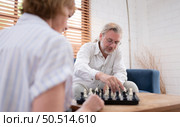 In the living room of the house, an elderly couple sits and relaxes. to begin playing chess together with a chess board. Стоковое фото, агентство Ingram Publishing / Фотобанк Лори