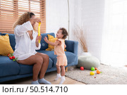 A little girl runs and plays with a small soap bubble that his mother blows for him to play with. In the living room of the house. Стоковое фото, агентство Ingram Publishing / Фотобанк Лори