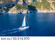 Aerial view of floating sailboat and rocky sea coast at summer sunny day. Top drone view of yacht, mountains, trees and blue water. Yachting in Sardinia, Italy. Tropical seascape with boat in ocean. Стоковое фото, агентство Ingram Publishing / Фотобанк Лори