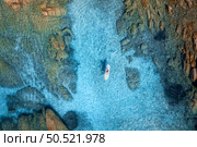 Aerial view of man on sup board in blue sea, rocks at sunset in summer. Man on floating canoe in transparent azure water. Kayak. Sardinia island, Italy. Tropical seascape. Active travel. Top view. Стоковое фото, агентство Ingram Publishing / Фотобанк Лори