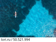 Aerial view of kayak with people in blue sea at summer sunny day. Man and woman on floating canoe in clear azure water. Sardinia island, Italy. Tropical landscape. Sup board. Travel. Top view of ocean. Стоковое фото, агентство Ingram Publishing / Фотобанк Лори