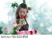 ?Young woman florist smelling a red rose in the flower shop. Стоковое фото, агентство Ingram Publishing / Фотобанк Лори